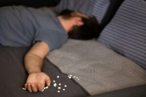 Man lying with pills on bed after suicide attempt