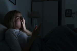 Sleepy woman lying in bed using smartphone, yawning. Insomnia, sleep disorder, social networks.